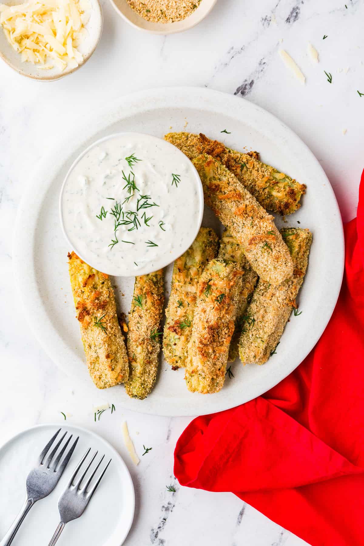 Top view of a plate of dill pickle fries and dill dip in a bowl, next to a couple forks.