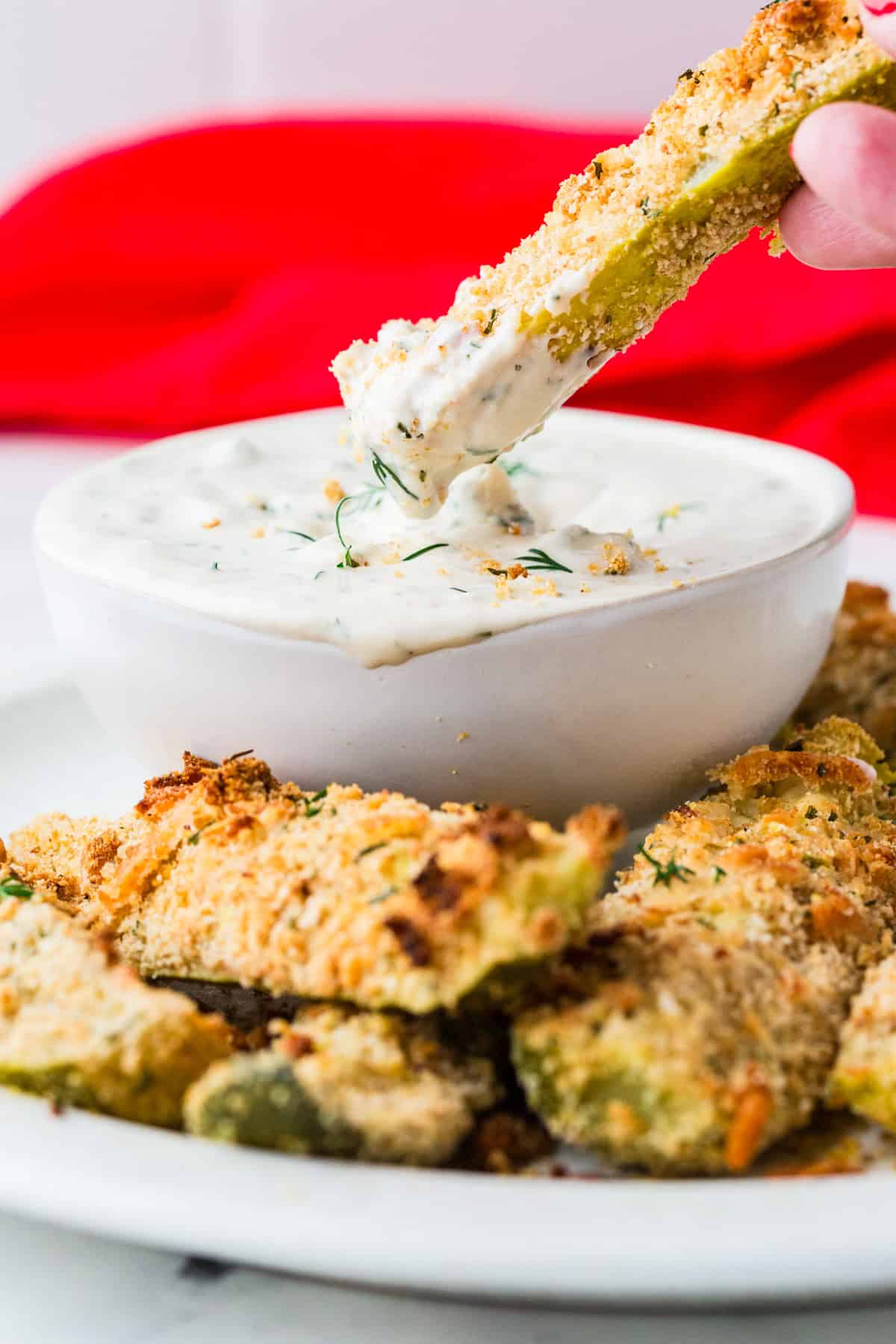 Fingers dipping a dill pickle fry into a small bowl of dill dip.