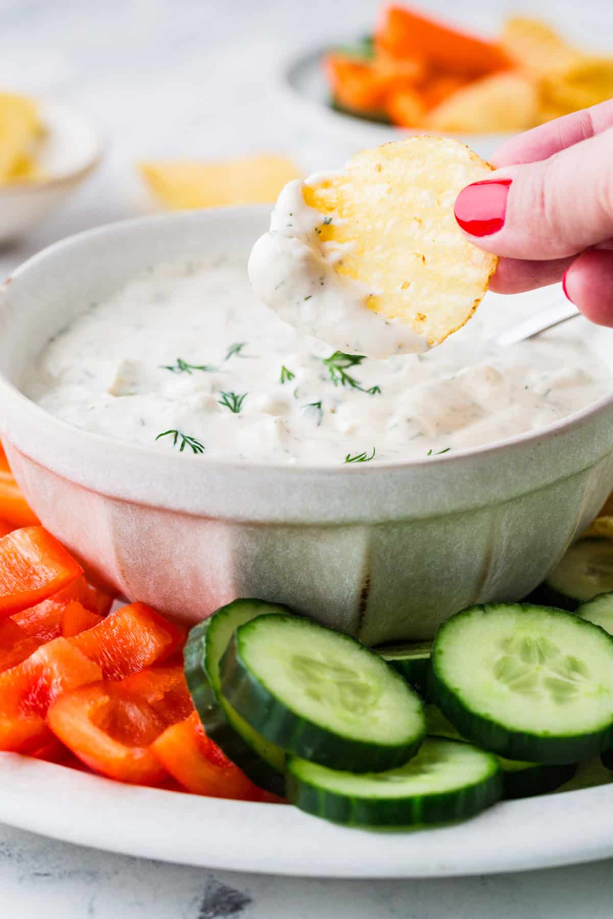 Fingers lifting a chip out of a bowl; the chip has a creamy yogurt dressing on it.