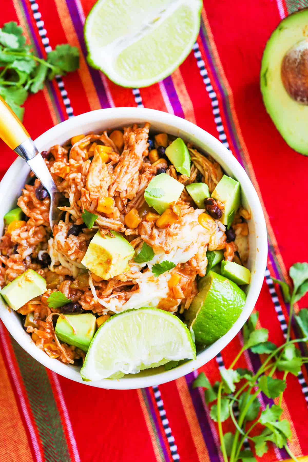 Delicious chicken and rice burrito bowl with avocado, lime, and fresh herbs on a colorful table.