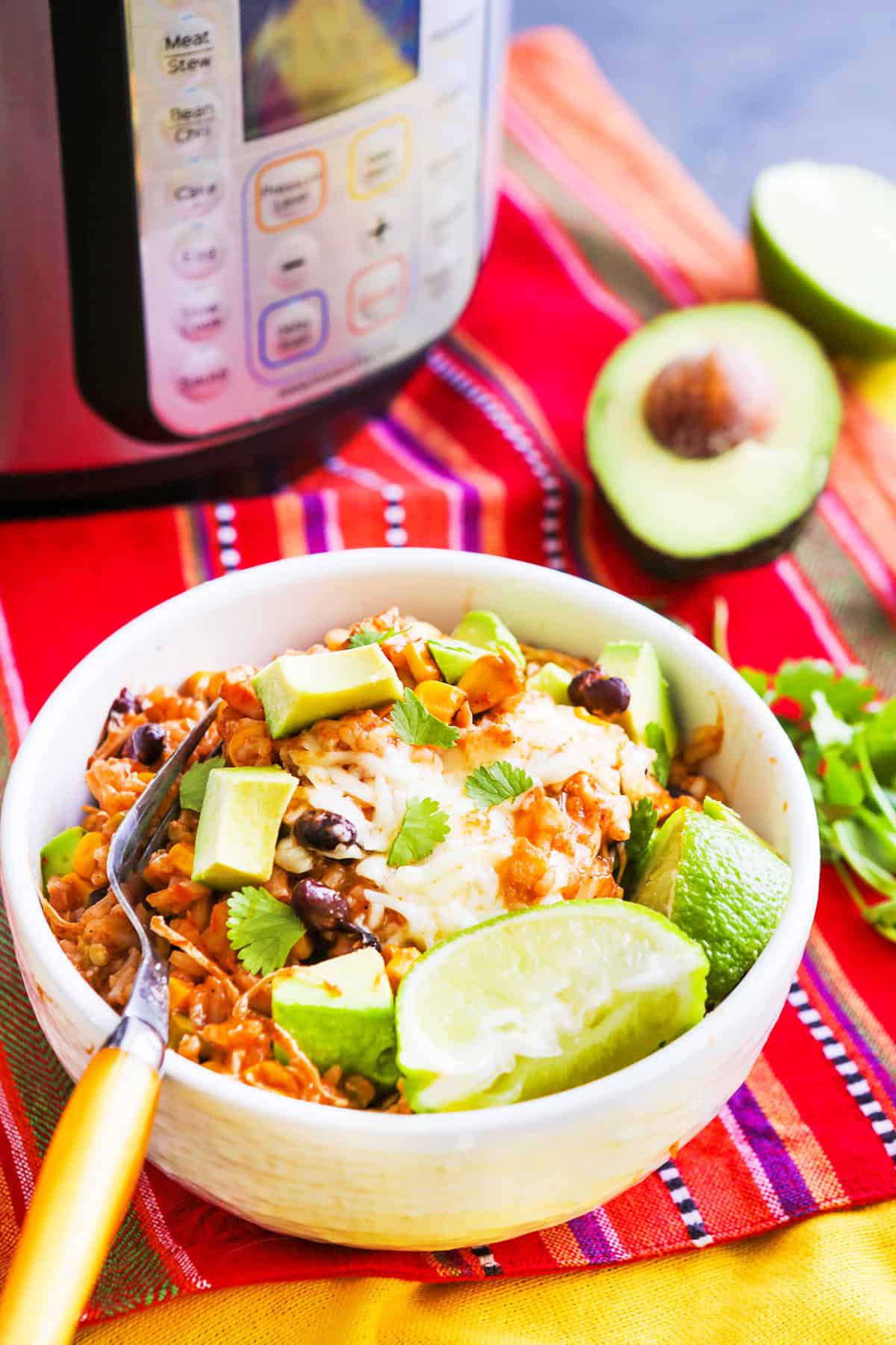 Healthy burrito bowl with avocado, lime, and cilantro served in a white bowl on a vibrant tablecloth.