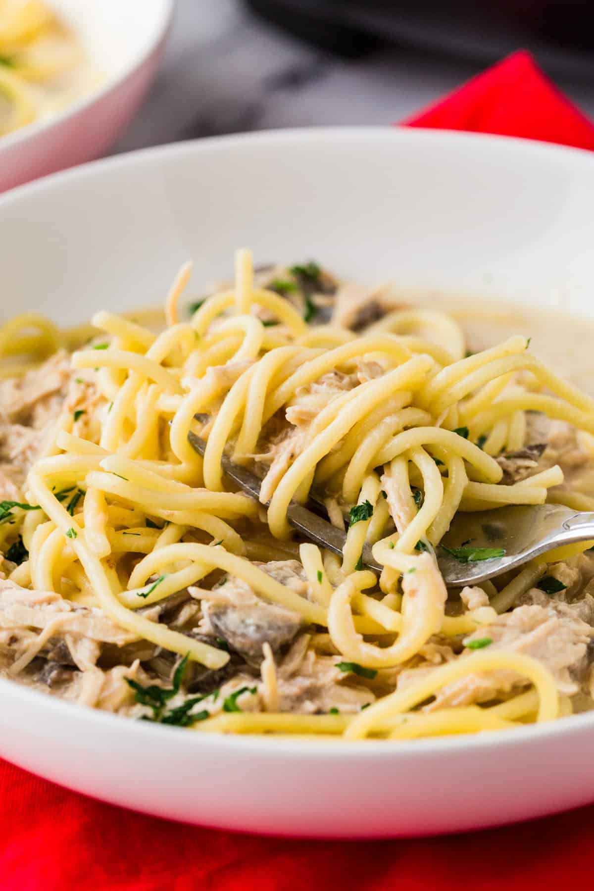 Close up of a fork with spaghetti noodles wrapped around it and bits of chicken hiding in the pasta.