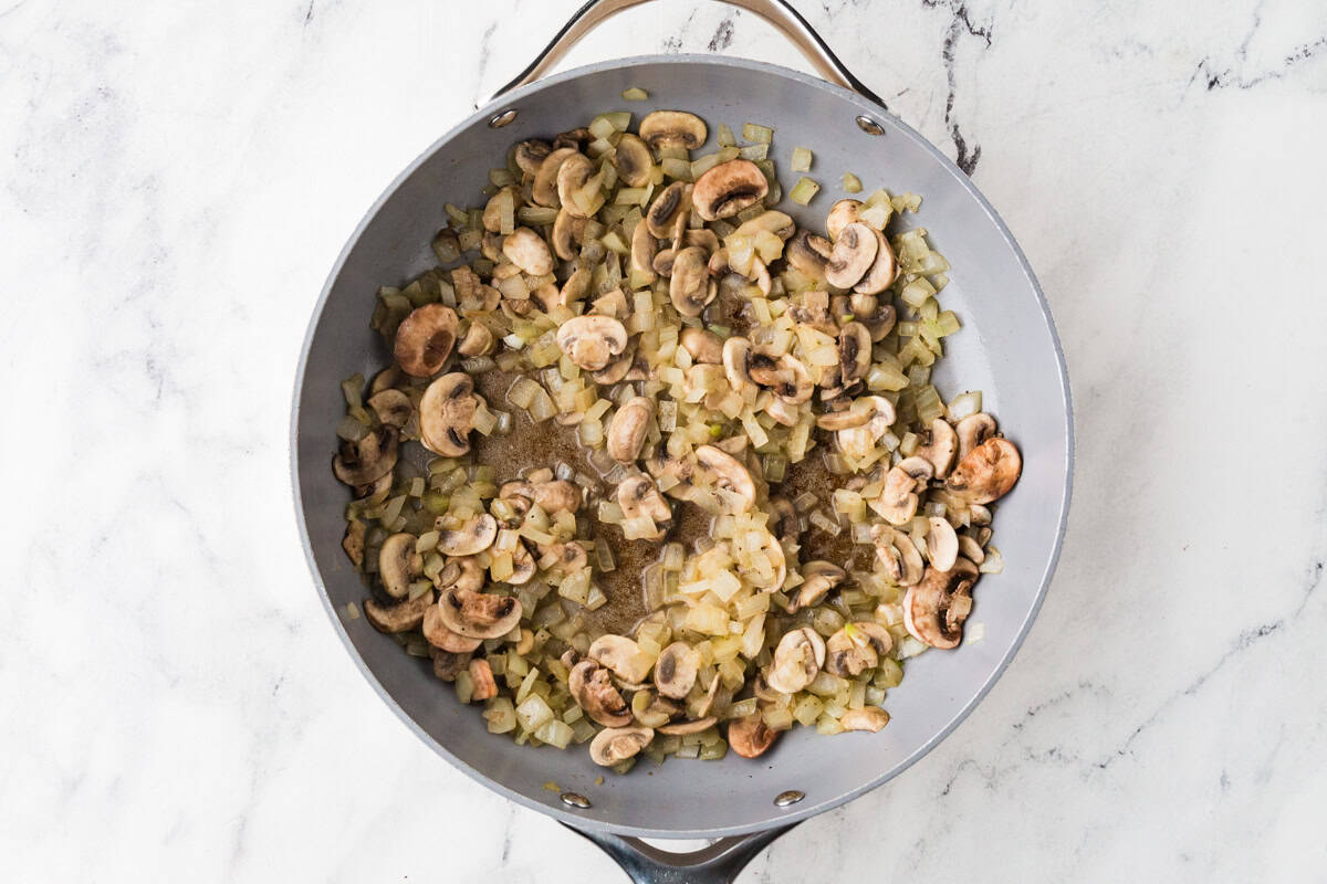 Skillet with cooked onions and mushrooms inside.