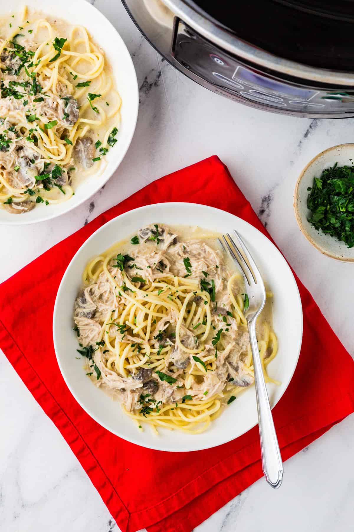 Looking down on a scene with a few plates of chicken tetrazzini, sitting next to a slow cooker.