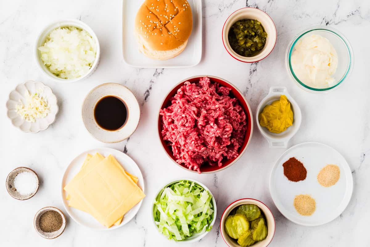 Ingredients for big mac sloppy joes in individual bowls lined up on a white counter.