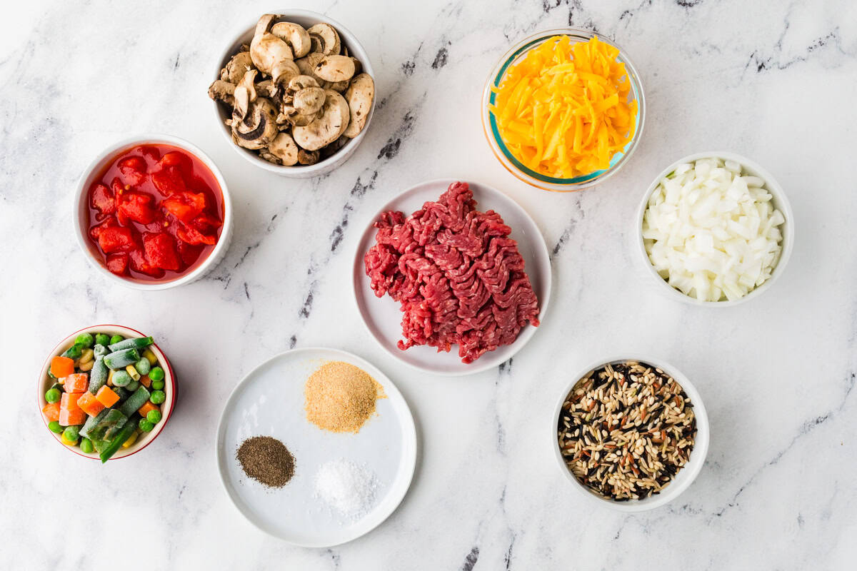 Ingredients for ground beef wild rice casserole in individual bowls lined up on a white counter.
