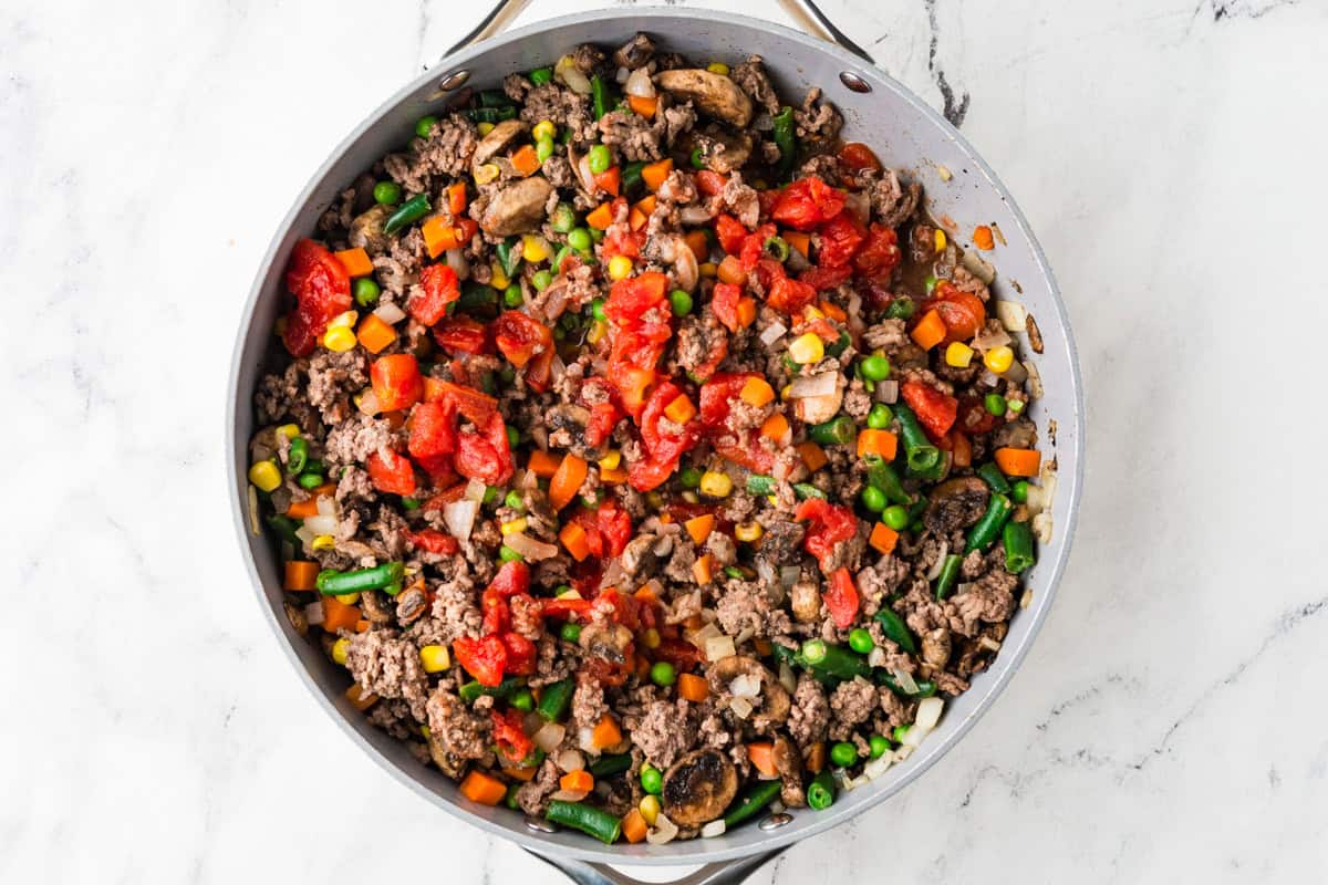 Skillet filled with cooked ground meat, veggies and canned tomatoes.