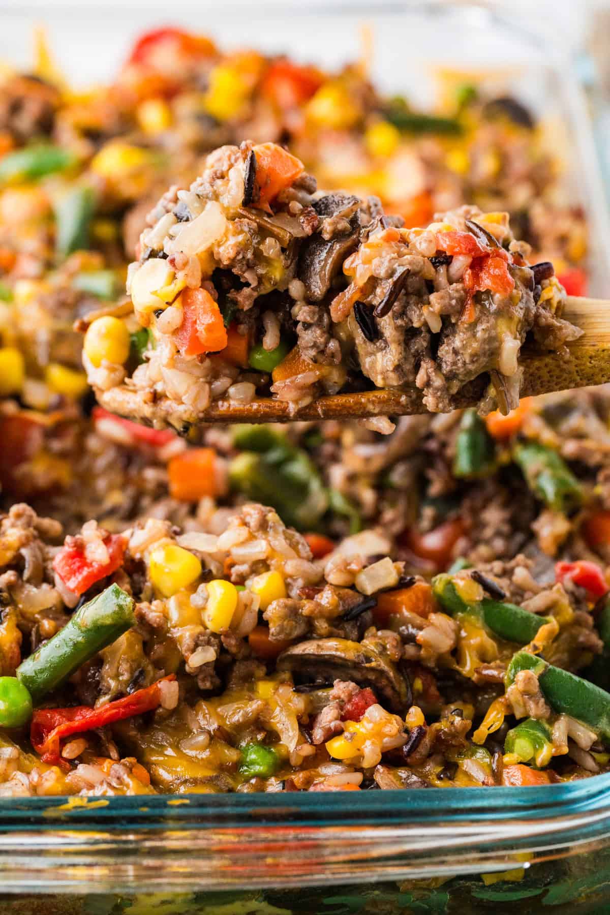 Wooden spoon with ground beef wild rice casserole on top, hovering over a pan of the final dish.