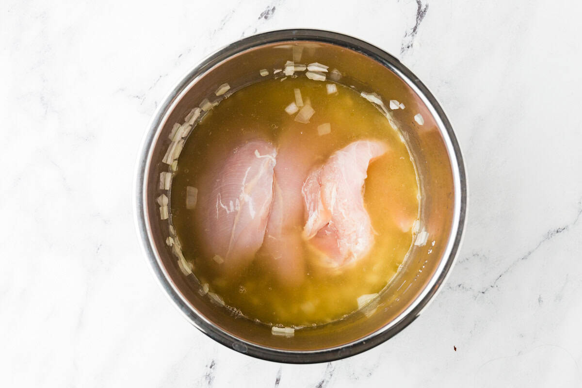 Uncooked chicken breasts in a broth mixture inside the pot of a pressure cooker.