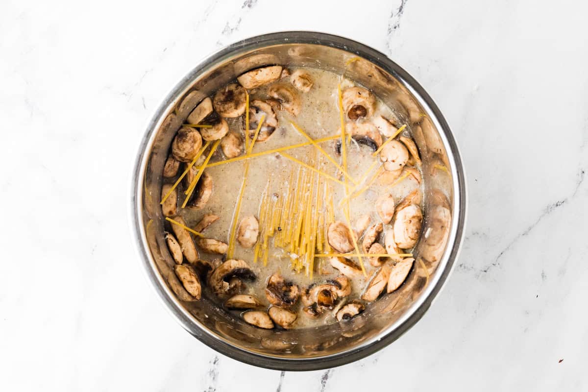 Spaghetti noodles on top of a liquid mixture with mushrooms in a pot.