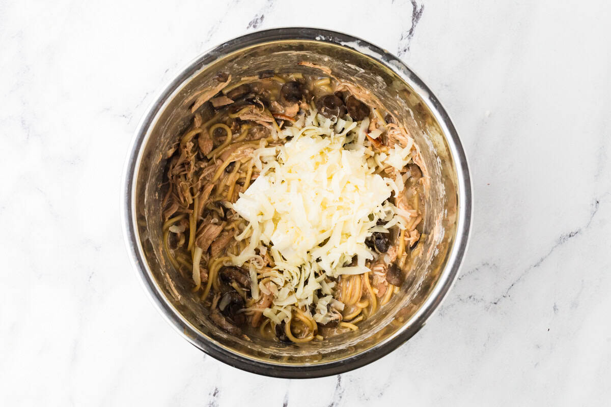 An Instant Pot with cooked pasta, mushrooms and shredded white cheese on top.