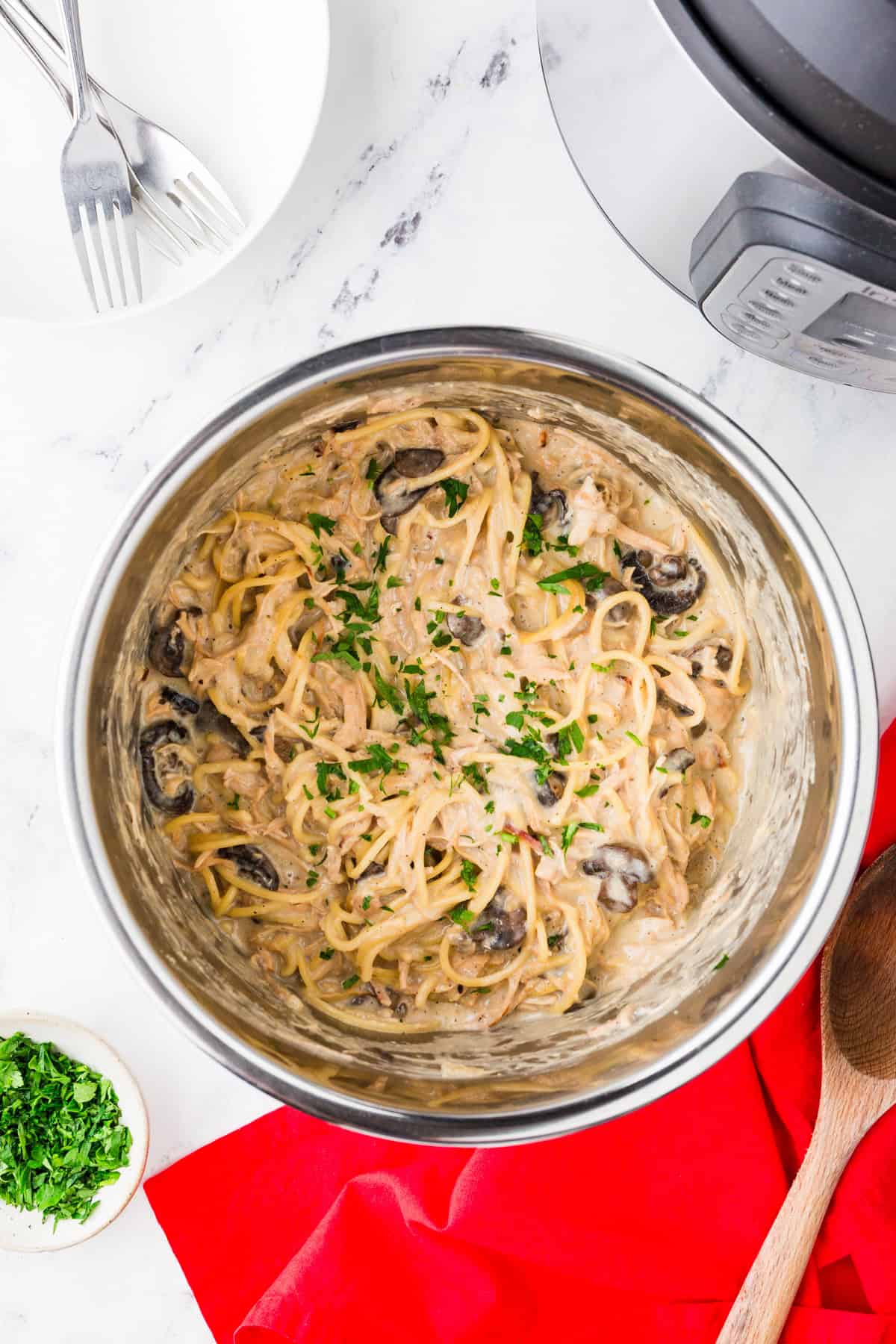 Top view of the inside pot of a pressure cooker filled with a pasta mixture, including parsley and mushrooms.