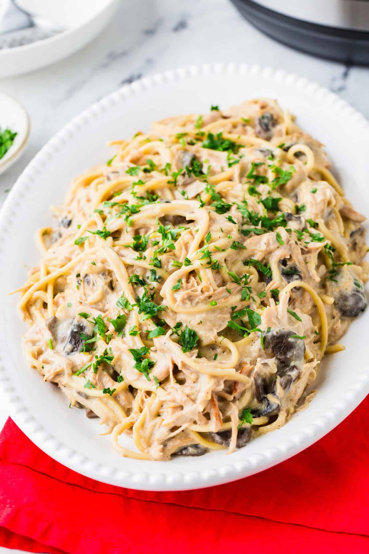Serving platter filled to the brim with a creamy pasta dish involving mushrooms and parsley.