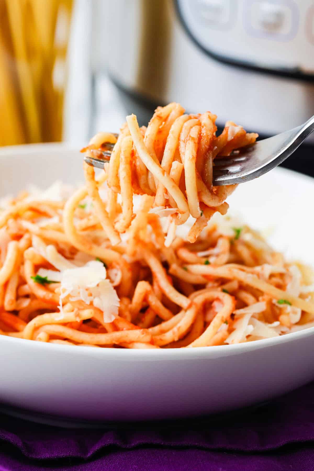 Fork holding saucy spaghetti noodles over a bowl.