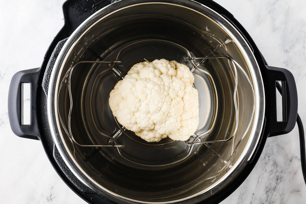Raw whole cauliflower on a trivet inside an Instant Pot.
