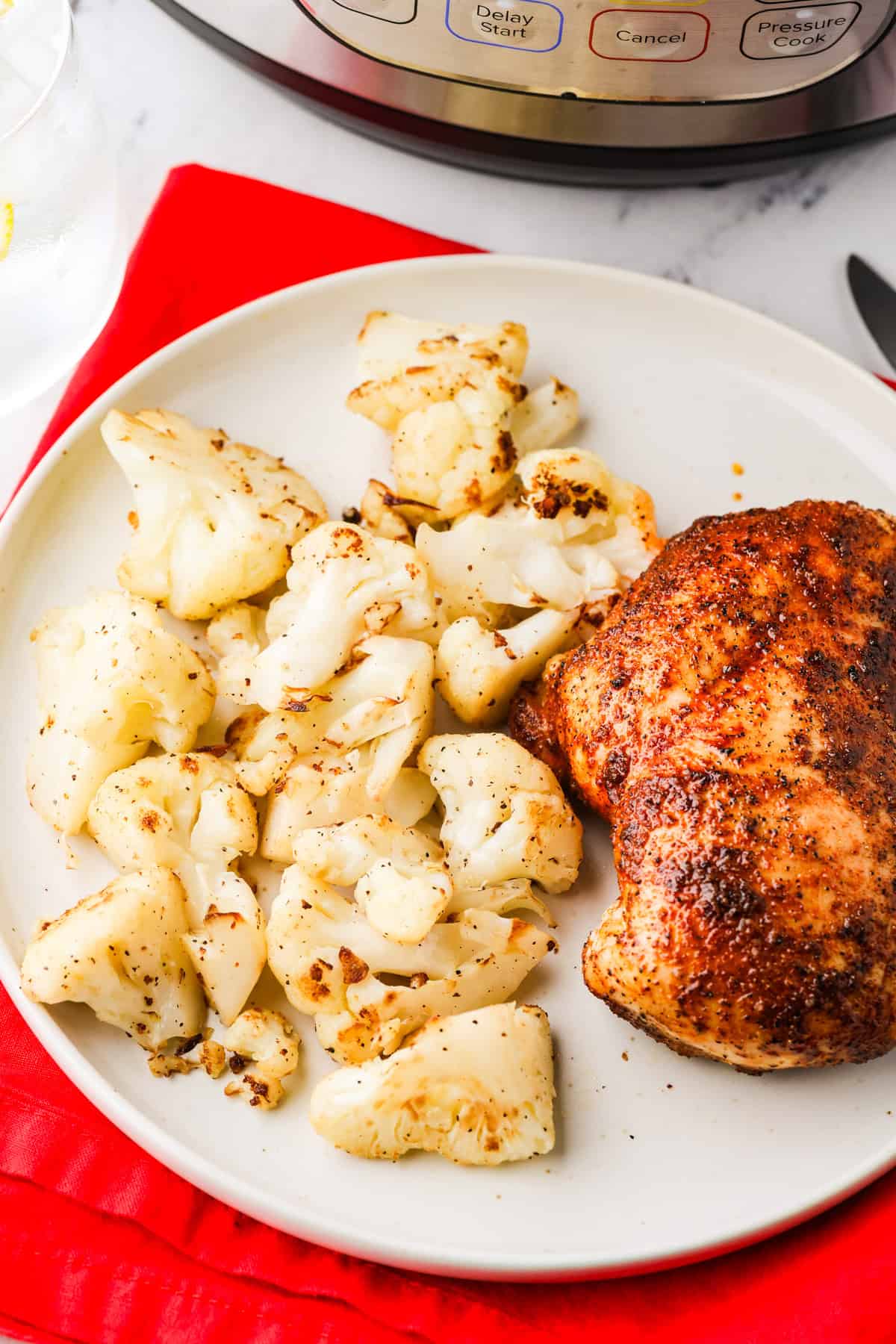 Plate of sauteed and golden cauliflower florets, next to a chicken breast.