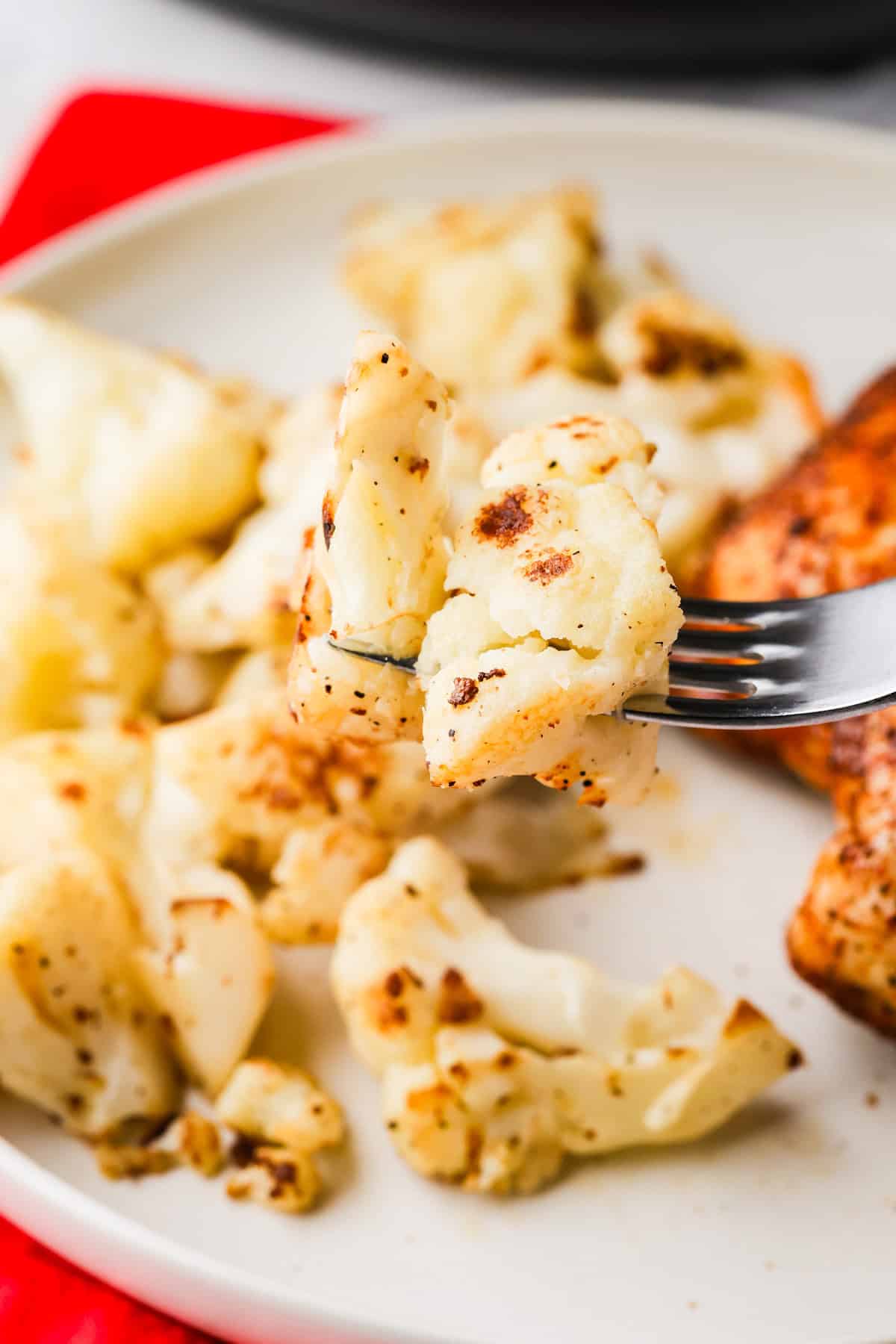 A fork lifting a bite of golden, cooked cauliflower florets over a plate of food.
