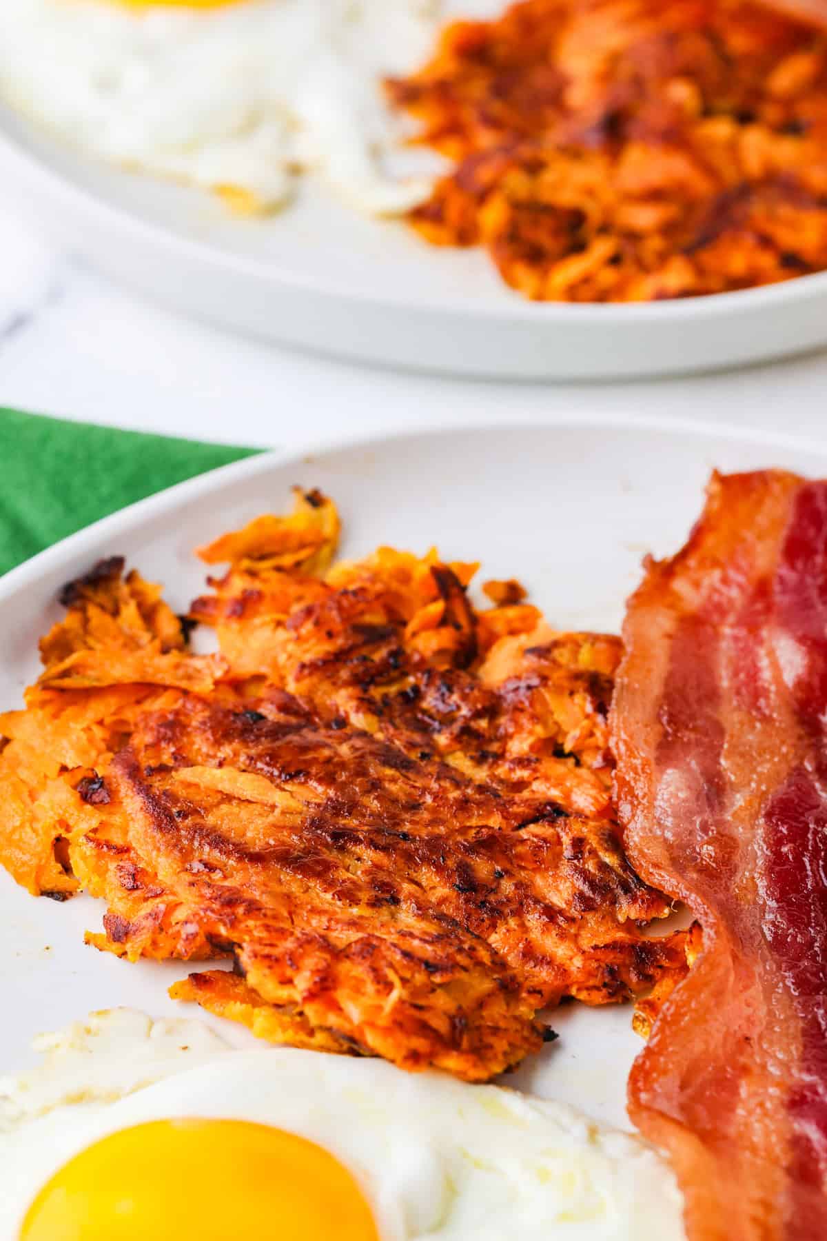 Sweet potato hash browns on a plate with bacon and an egg.