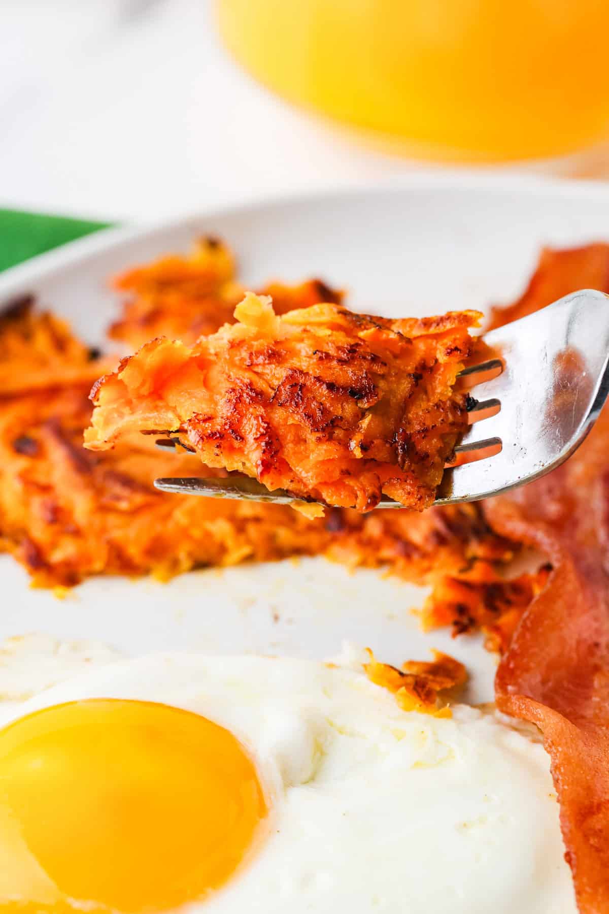 Fork holding a bite of sweet potato hashbrowns over a plate.