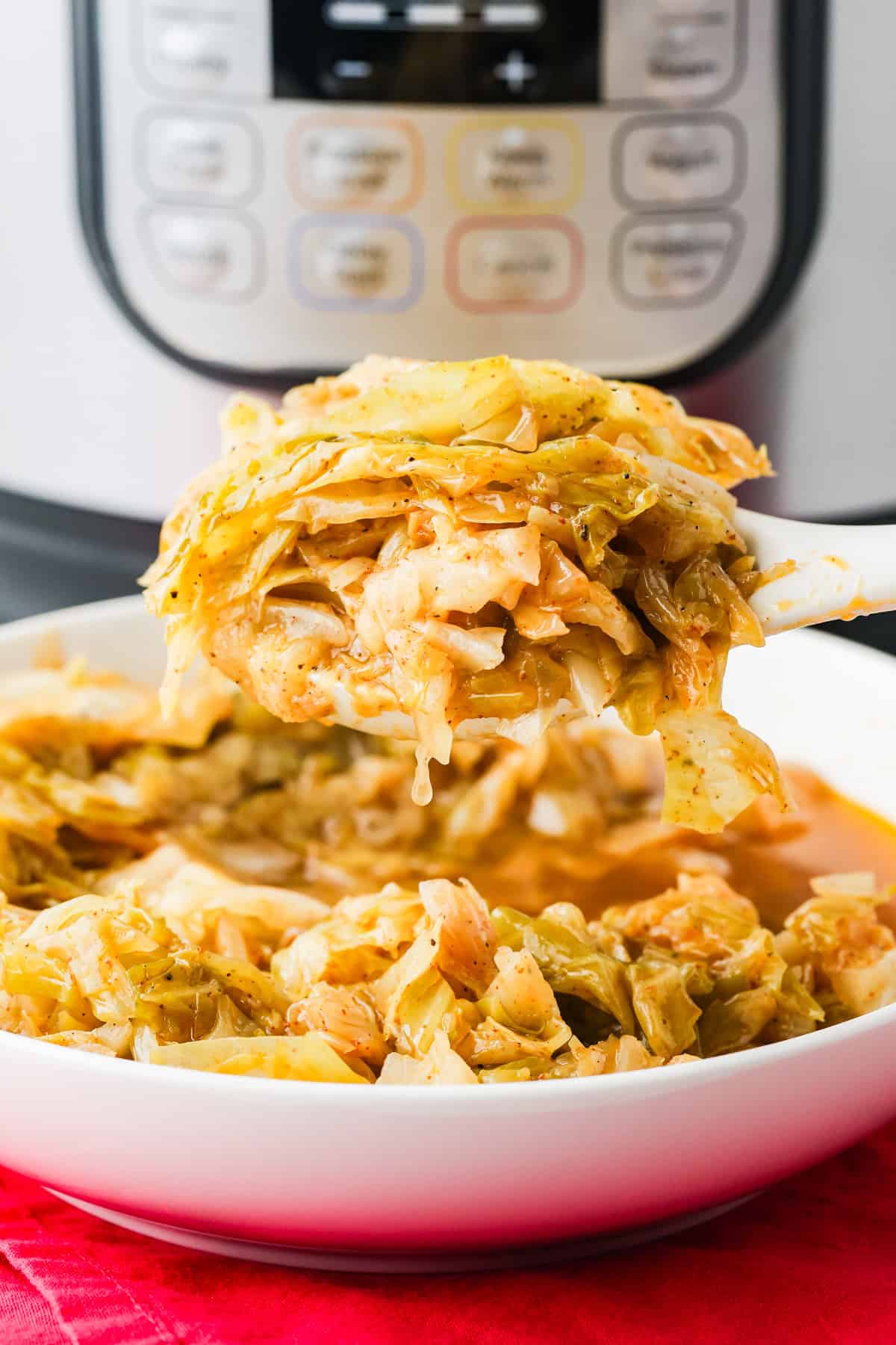 Spoon holding chopped cabbage over a serving bowl, with a pressure cooker in the background.