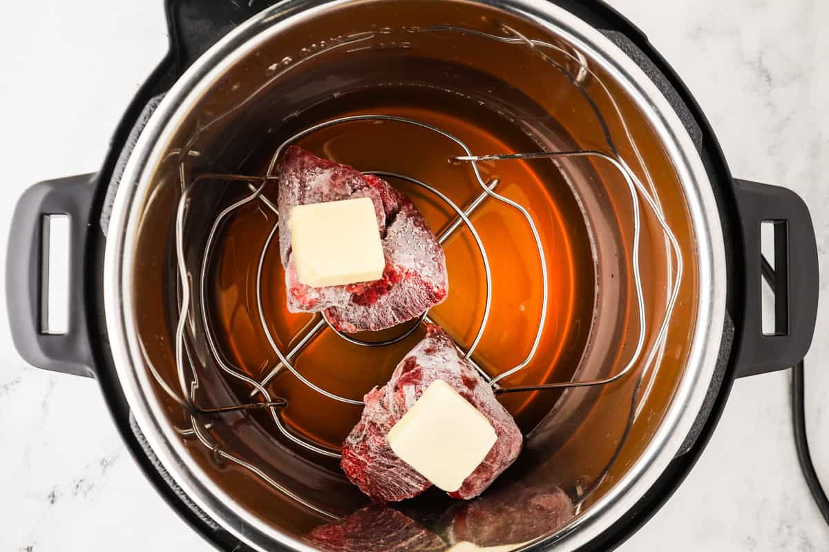 Frozen steaks on a trivet with pats of butter on each, in a pressure cooker.