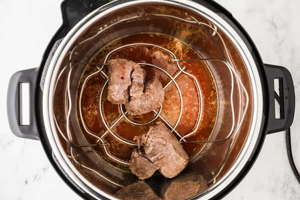 Cooked steaks on a trivet inside an Instant Pot.