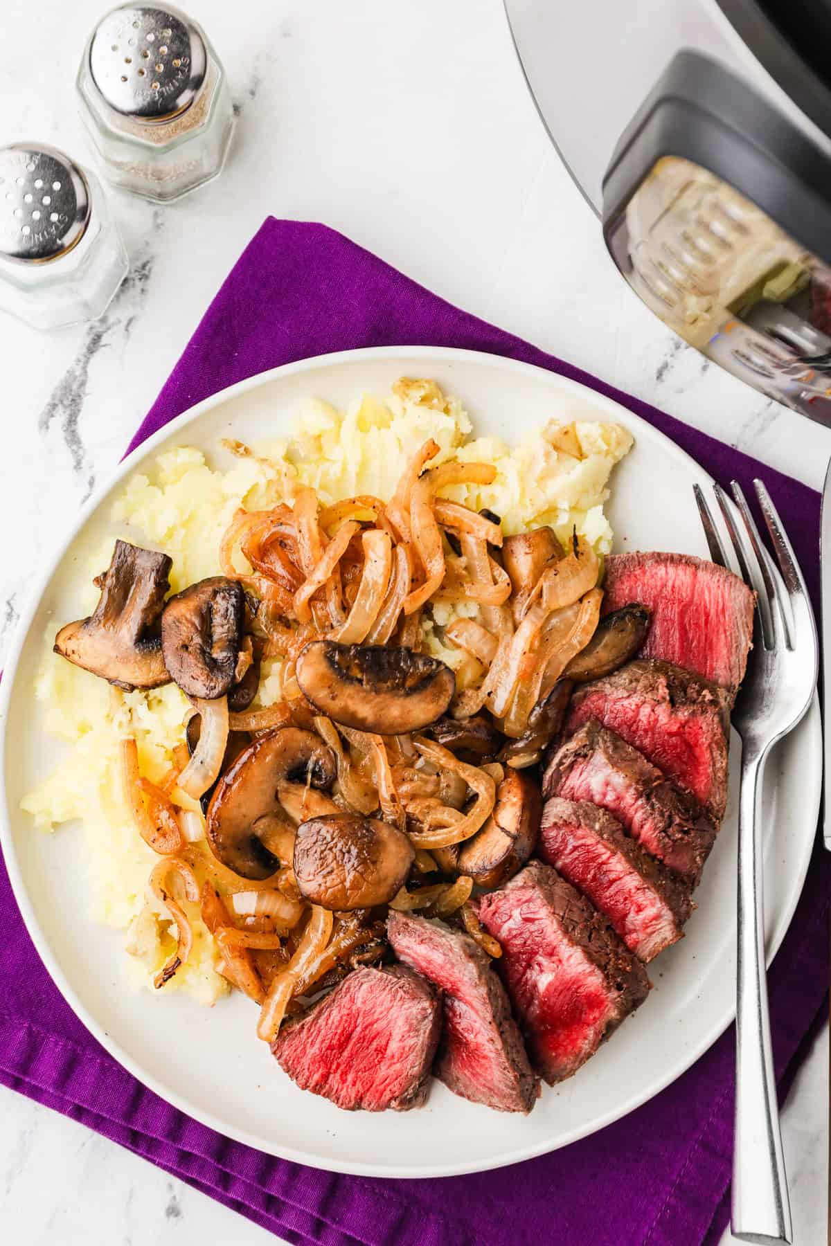 Top view of a plate of sliced steak, mushrooms and onions.