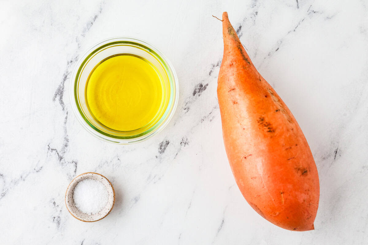 A sweet potato next to some oil and a small bowl of salt.