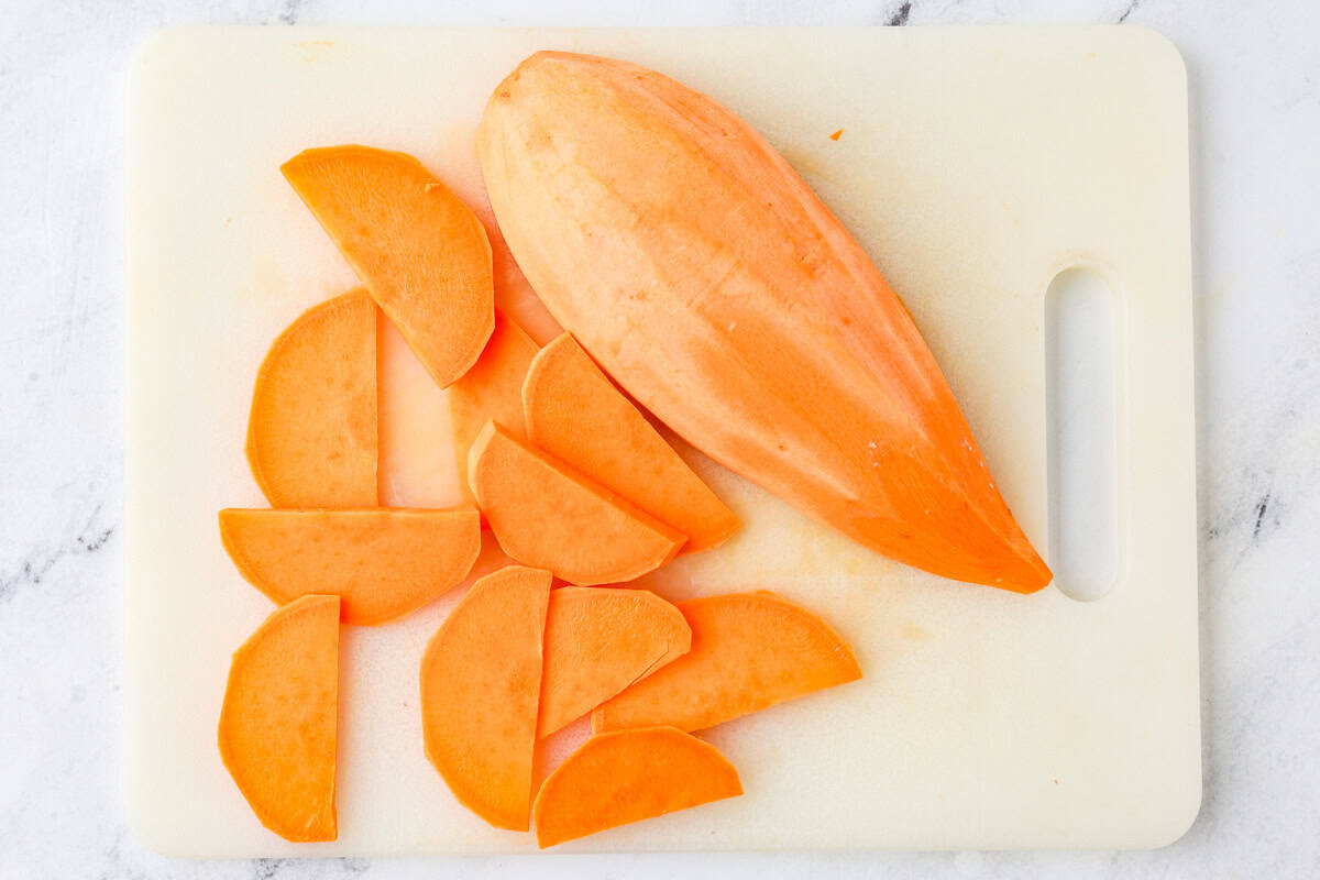 Half of a sweet potato on a cutting board, next to a few slices that have been cut.