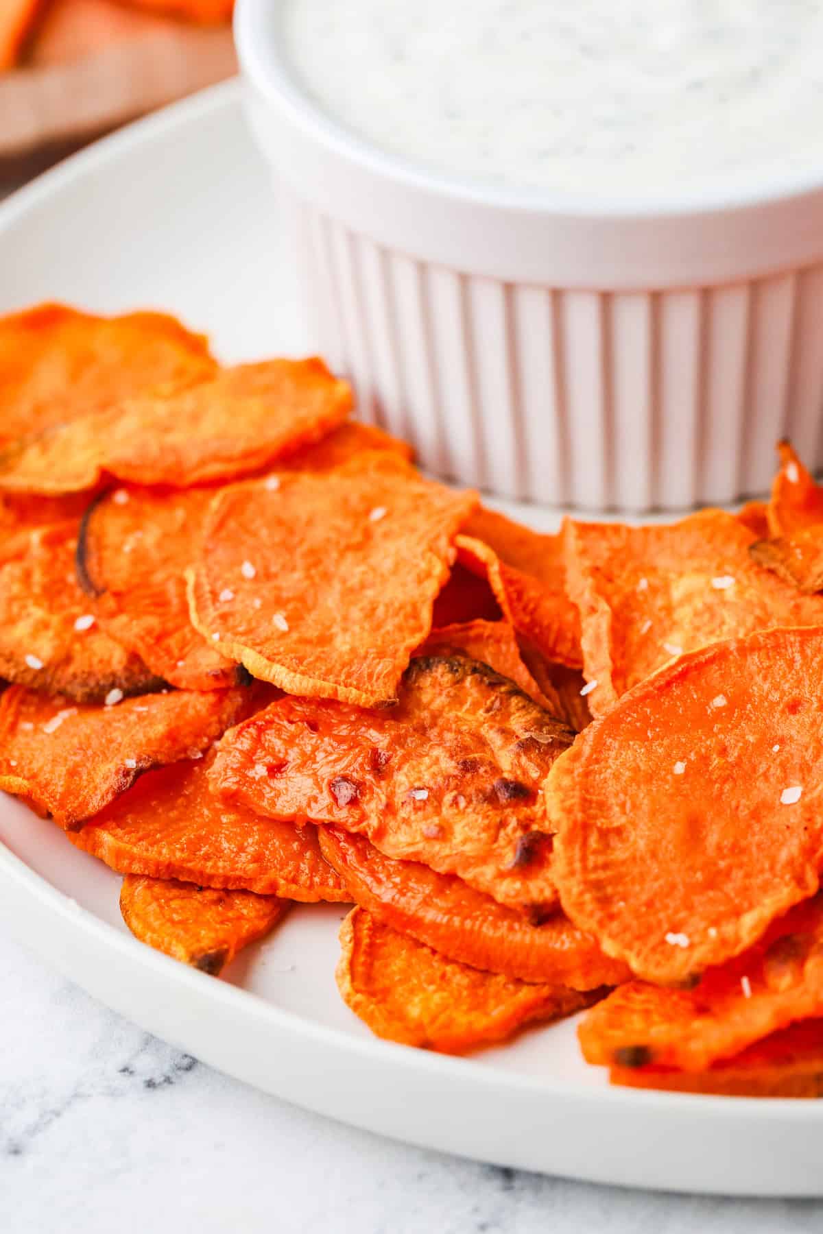 Sweet potato chips on a serving plate, next to a white dip.