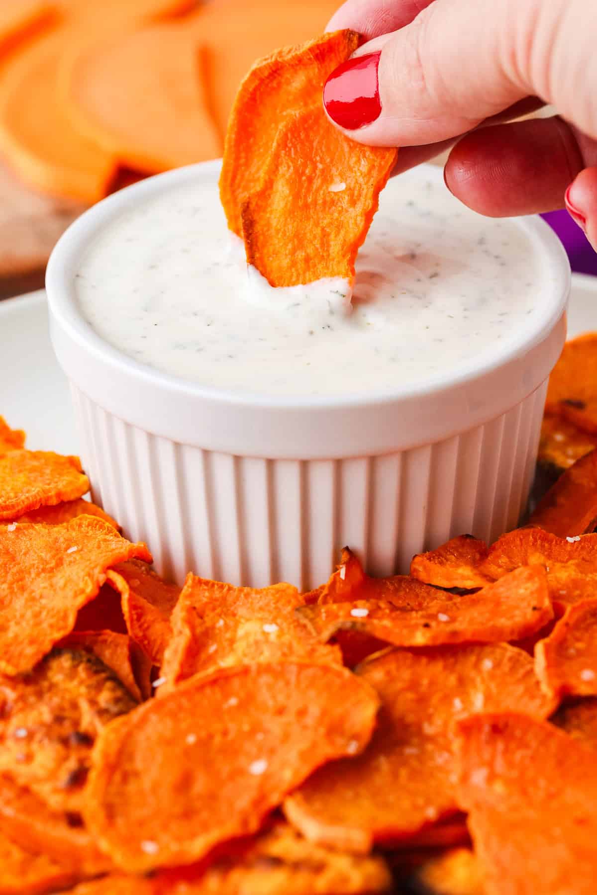 Hand dipping a sweet potato chip into a dip.