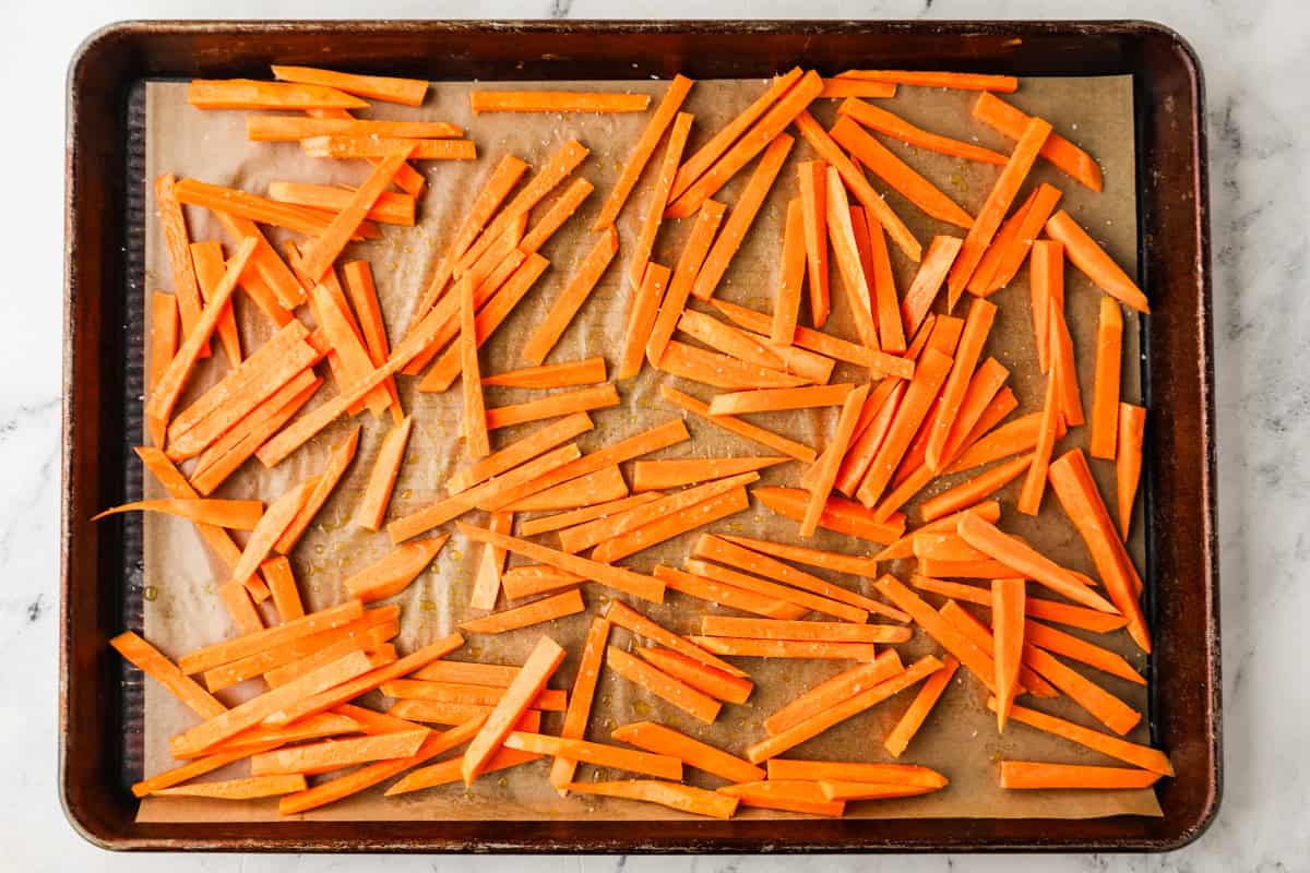 Top view of sweet potatoes cut into fry form, on a baking sheet.