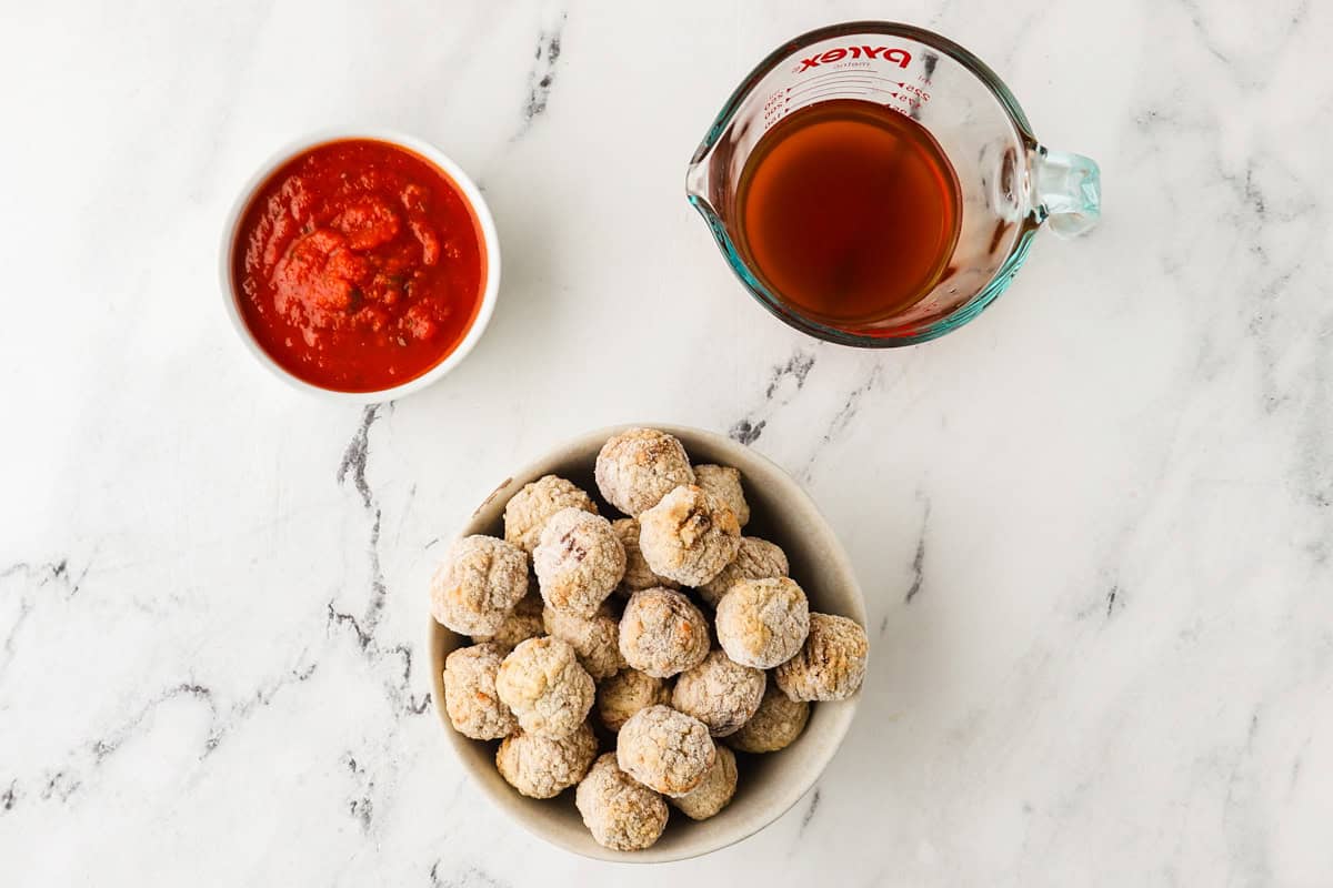 Chicken meatballs with tomato sauce and broth on a white marble surface.