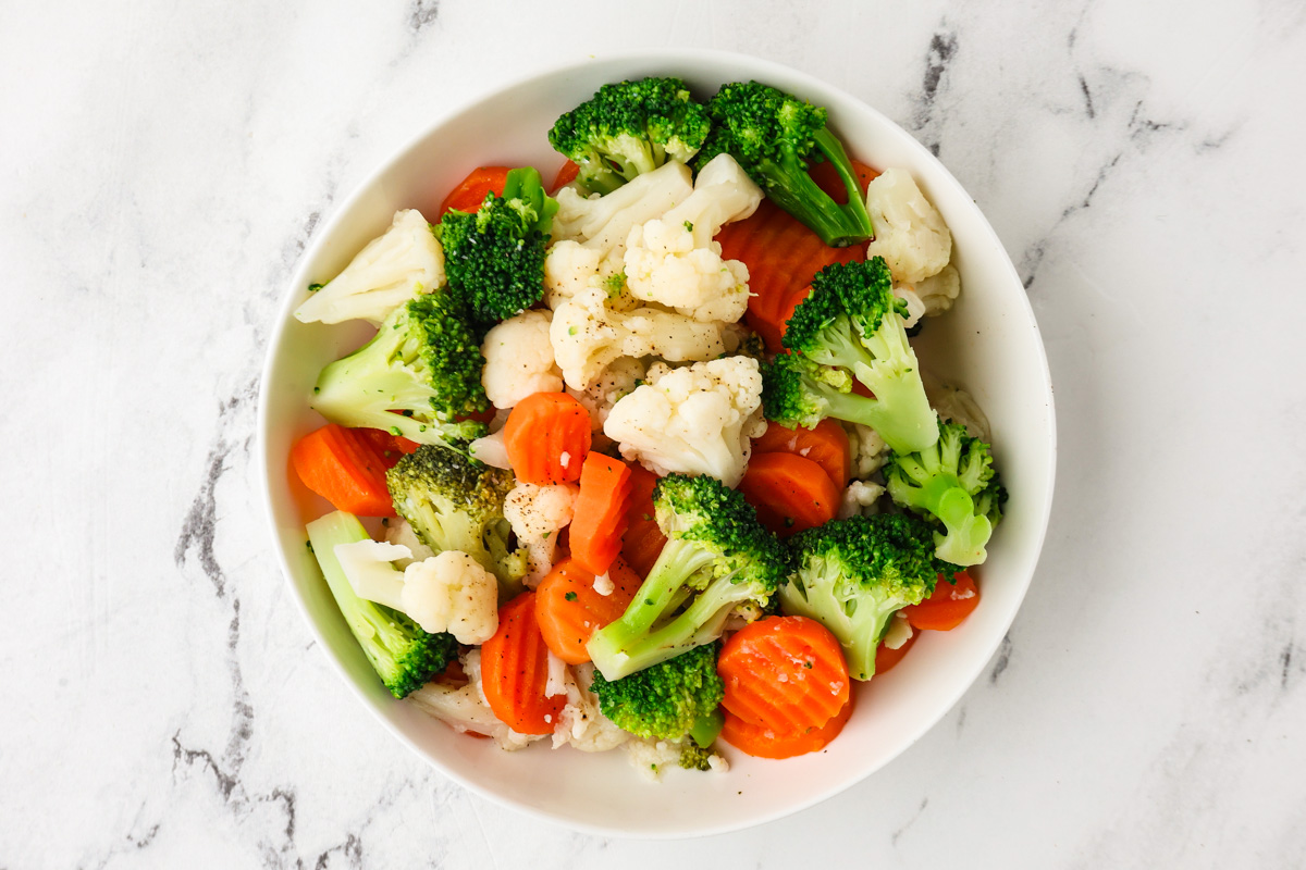 Healthy steamed frozen broccoli, cauliflower, and carrots in a white bowl.