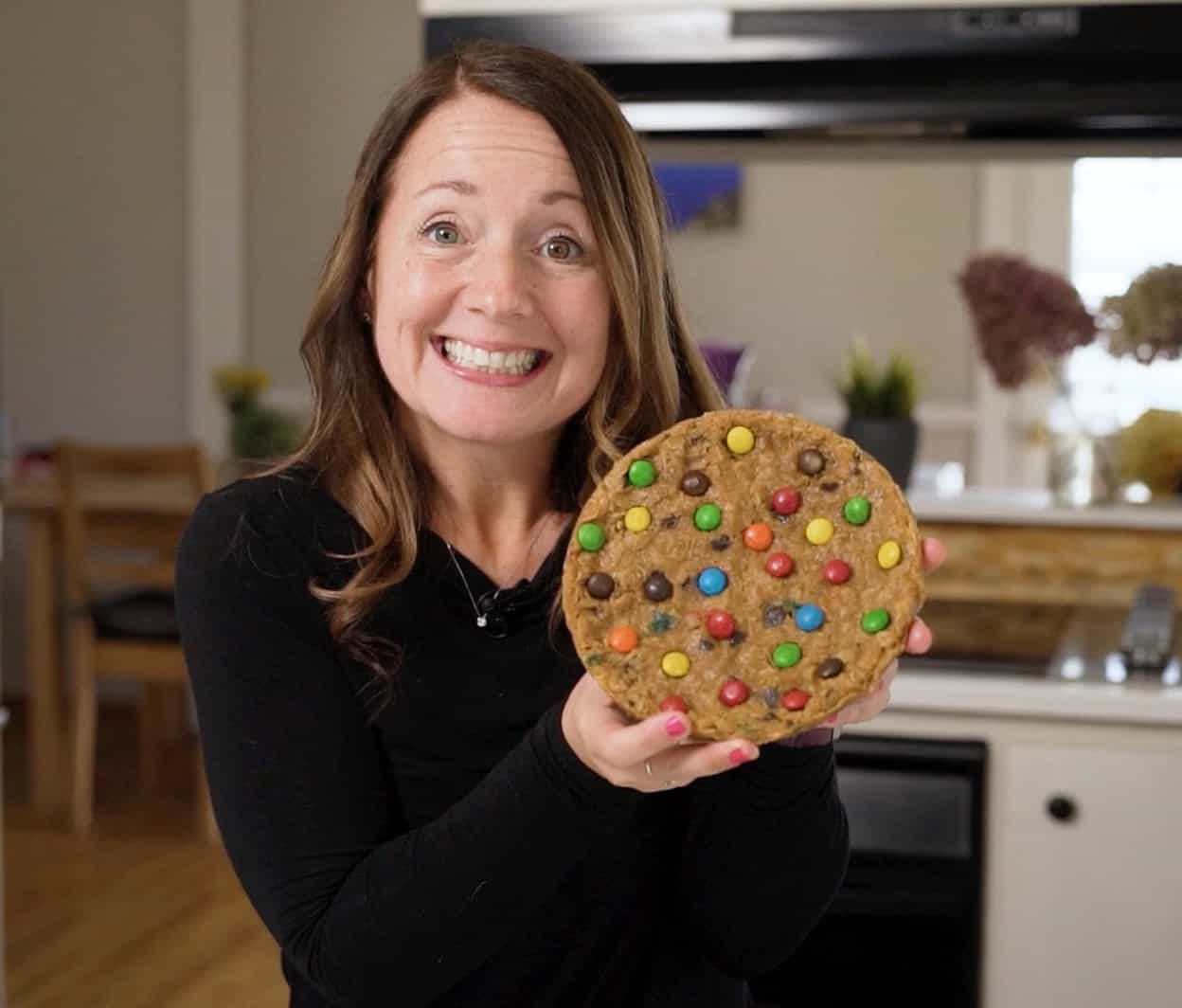 Megan Porta, Instant Pot recipe creator, holding a large cookie decorated with rainbow candies, smiling warmly.