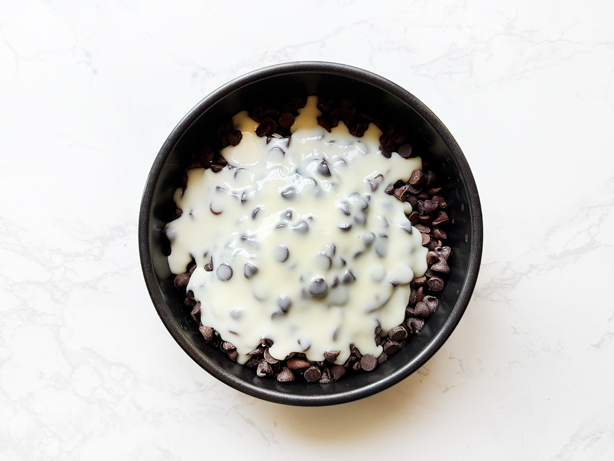 Chocolate chip cookie dough with white chocolate chips in a black bowl.