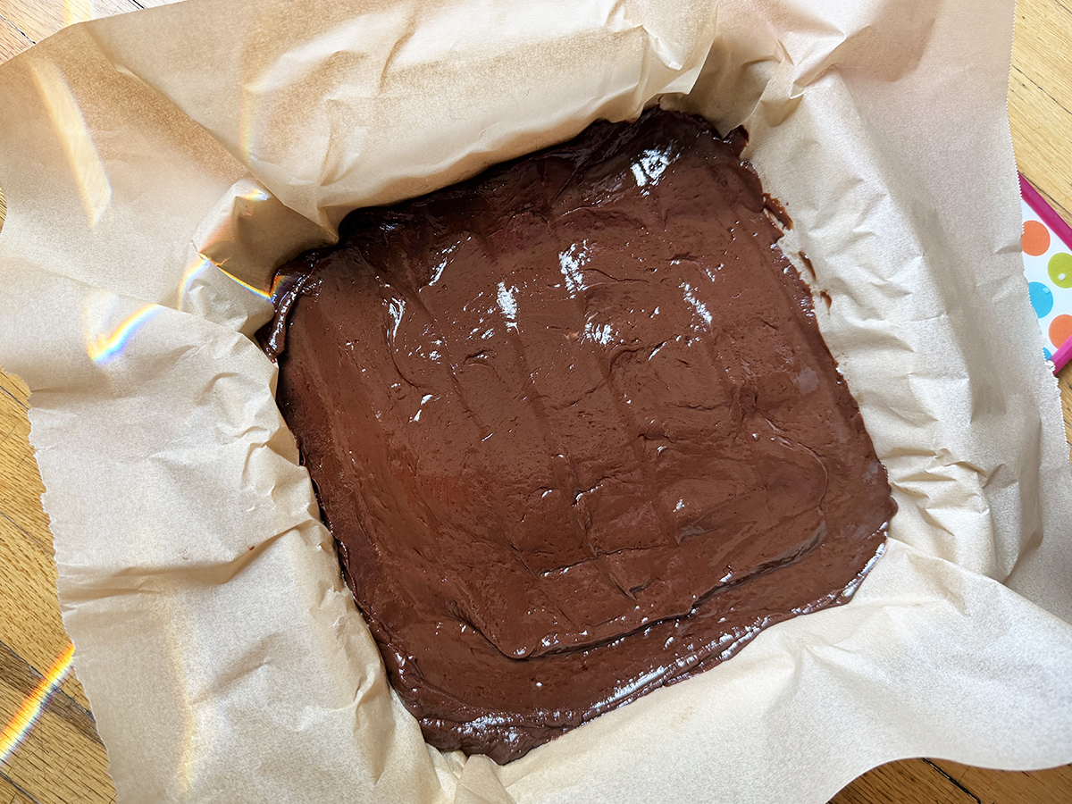 Freshly baked chocolate brownie in a parchment-lined pan, ready to be sliced.