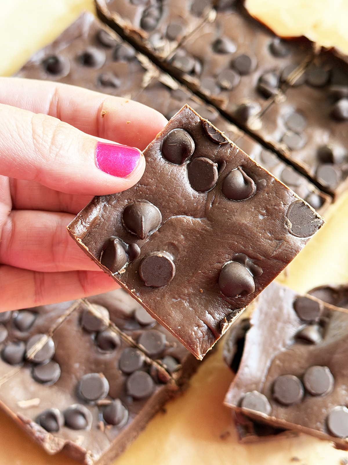 Close-up of chocolate chip cookie bars with melted chocolate chips, hand holding one piece.