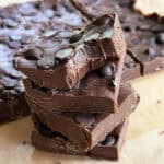 Close-up of homemade chocolate fudge topped with chocolate chips, stacked on parchment paper.