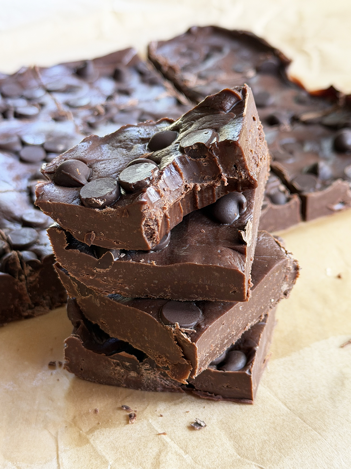 Close-up of homemade chocolate bark topped with chocolate chips, stacked on parchment paper.