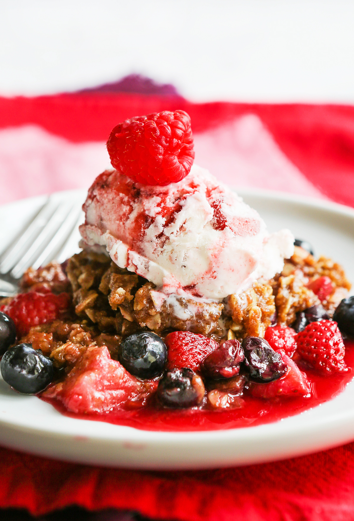 Serving of Instant Pot berry crisp with a scoop of ice cream and a raspberry on top.