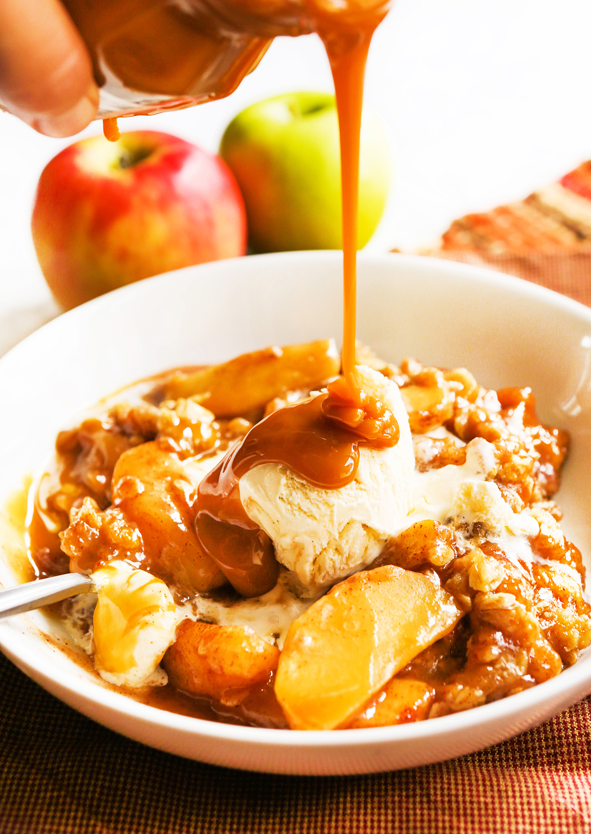 Caramel drizzling over a bowl of apple crisp and vanilla ice cream.
