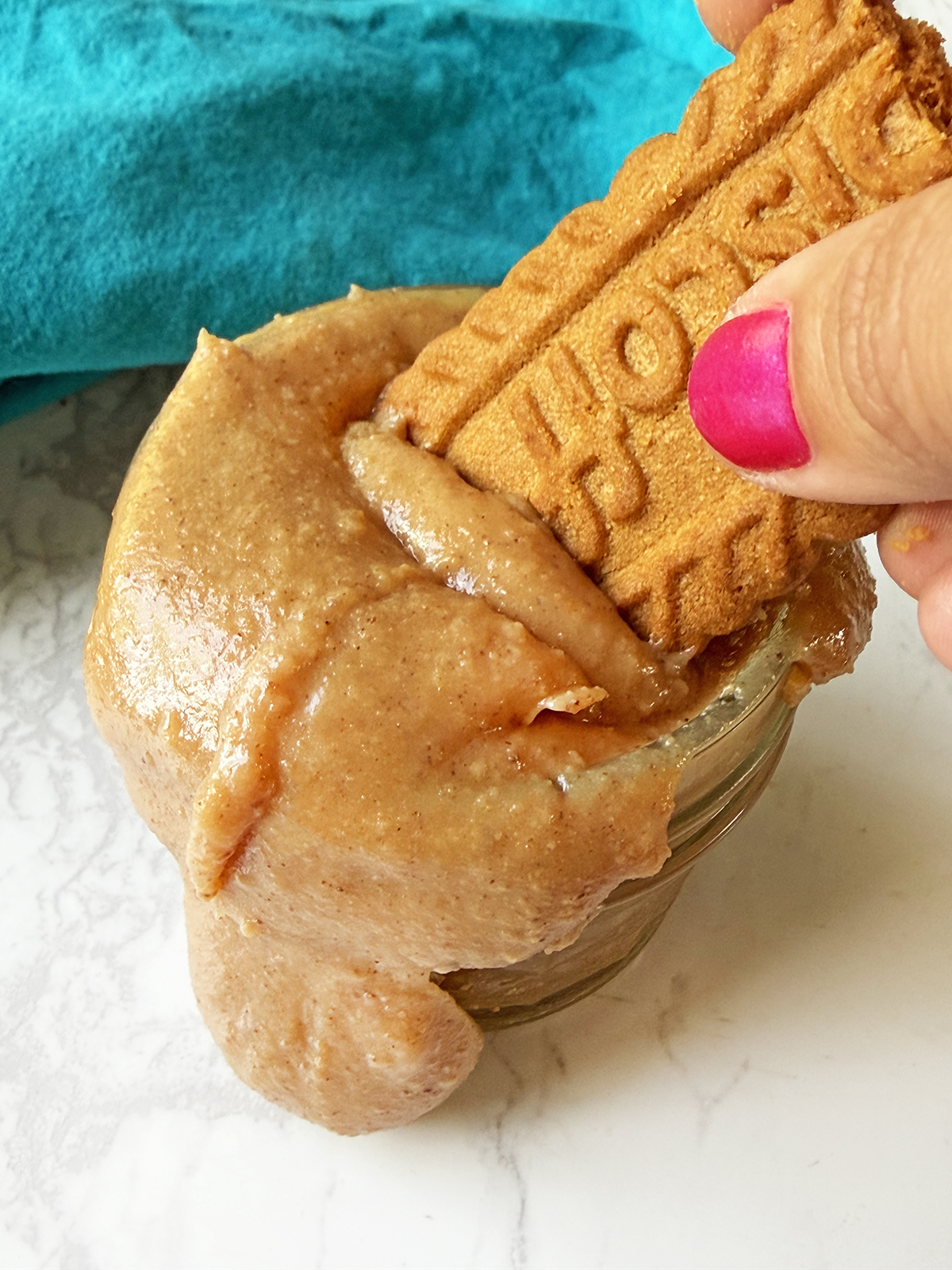 Close-up of a cinnamon roll topped with a biscuit and cookie, held by a hand with pink nail polish.