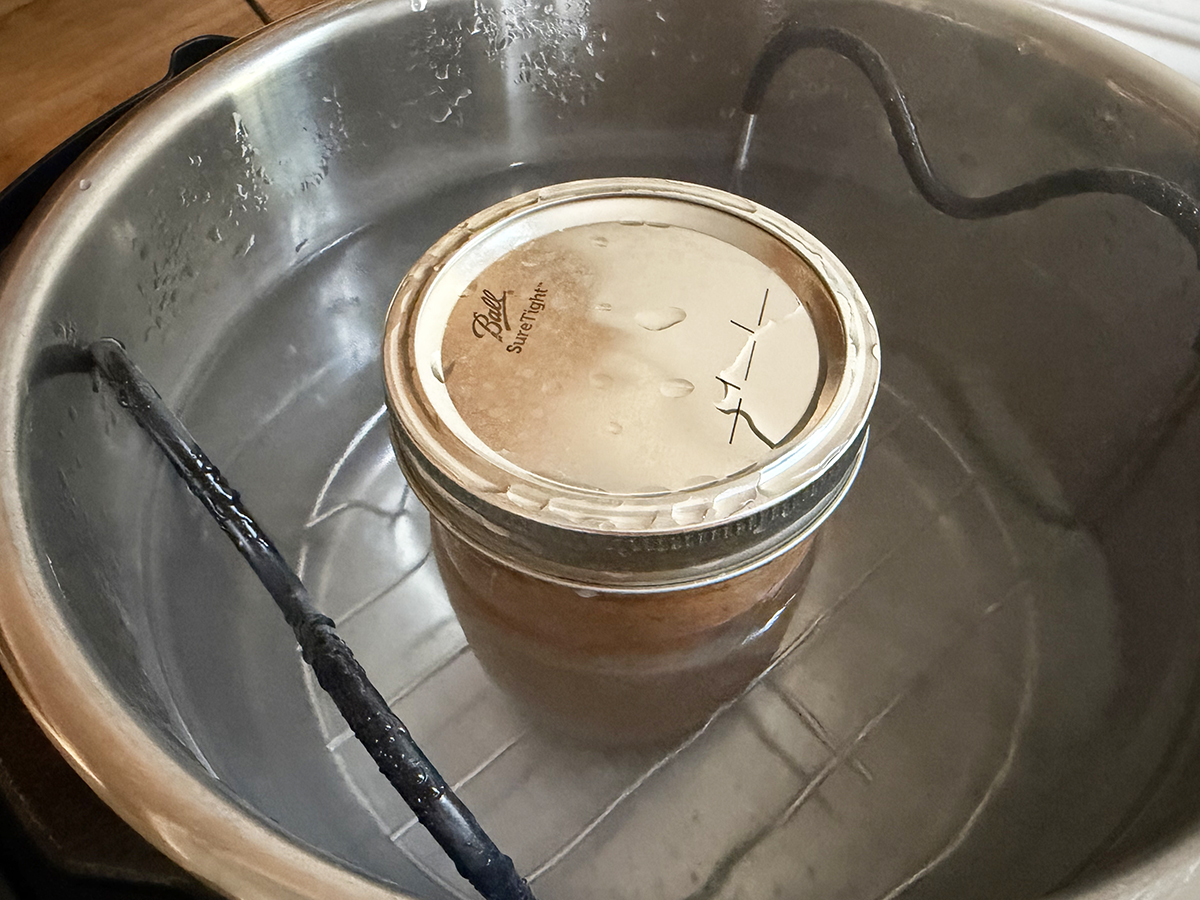 Mason jar submerged in water bath for home canning process.