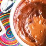 Rich chocolate pudding in a white bowl, served with a colorful woven placemat and silver spoon.