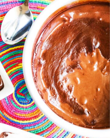 Rich chocolate pudding in a white bowl, served with a colorful woven placemat and silver spoon.