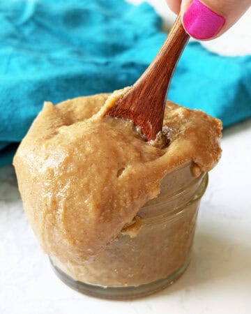 Creamy homemade dulce de leche in a glass jar with a wooden spoon.