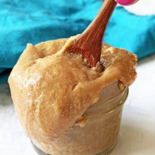 Creamy homemade dulce de leche in a glass jar with a wooden spoon.