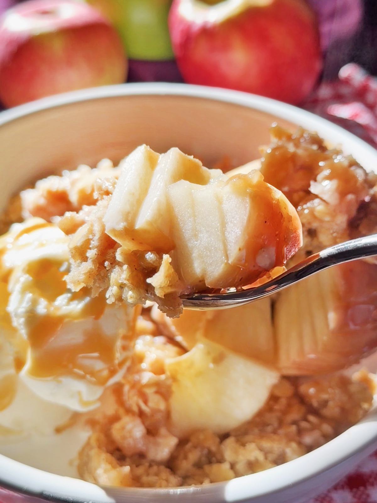 Bowl of apple crisp with spiral-cut apples and caramel sauce, with apples in background.