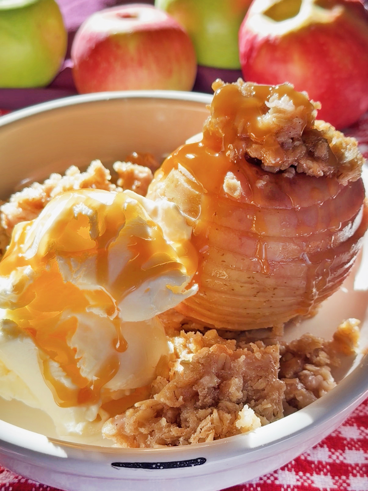 Baked apple with caramel sauce and vanilla ice cream in a bowl with apples in background.